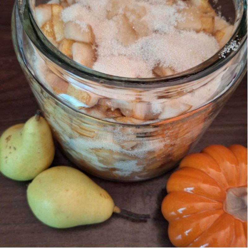 Birnen-Shrub-Ansatz aus Birnen und Rohrohrzucker, hier mit zwei grünen Birnen und einem kleinen orangefarbenem Kürbis Titletext: großes Glas mit einem Birnen-Shrub-Ansatz Fotocredit Maria Squarra @Dalslandliebe